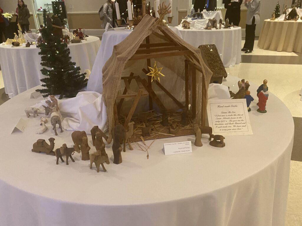 A nativity scene made from wood and burlap. Alongside Mary, Joseph, and Baby Jesus, the three wise men, an angel, Shepards, and some animals are depicted as well. 